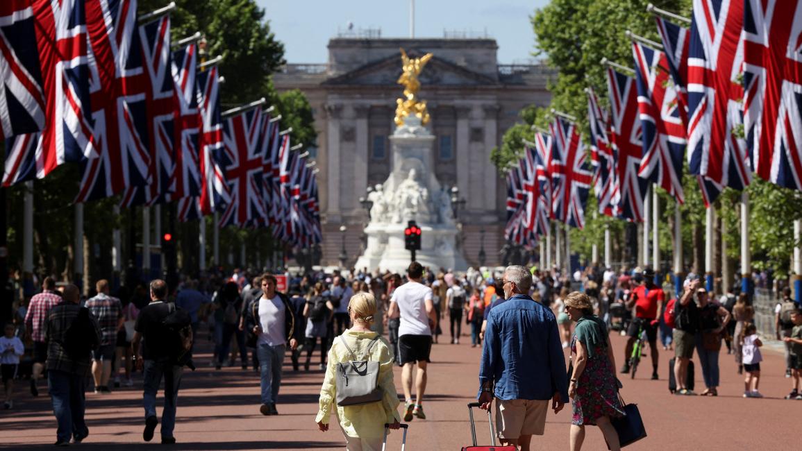 سياح يتفقدون ساحة قصر باكنغهام المزين بالأعلام (كيفن كومبس/رويترز)