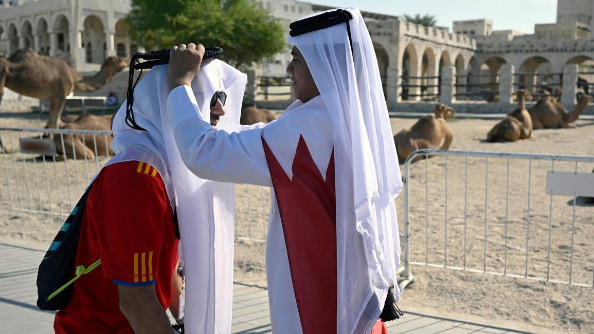 شاب قطري يساعد مشجعاً إسبانياً على ارتداء غطاء رأس (ألفريدو إستريلا / Getty)