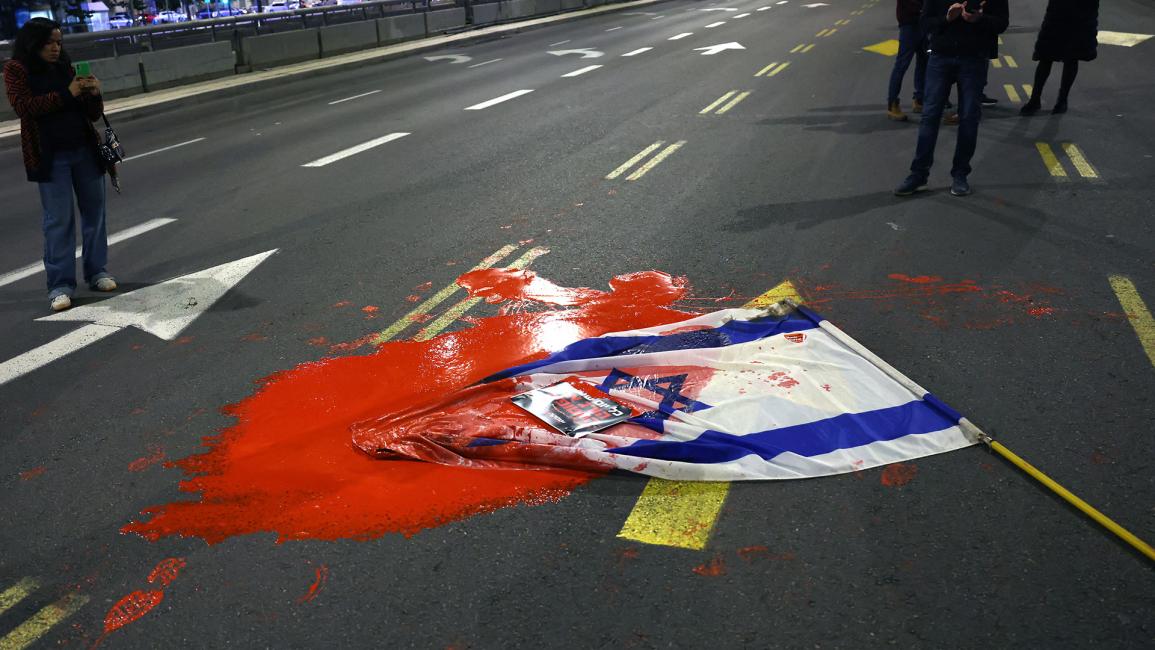 علم الاحتلال ملقىً على الأرض وملطخ بدهان أحمر تعبيراً عن قتل محتجزين على يد جيش الاحتلال (أحمد الغربلي/ Getty)