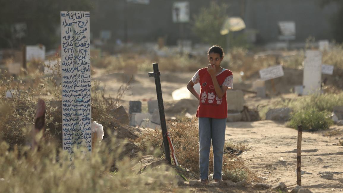 طفلة تقف أمام قبر جماعي لشهداء من أسرة واحدة (داود أبو الكاس/الأناضول)