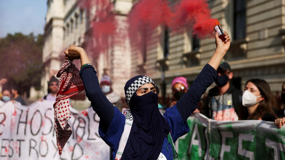 متظاهرة تحمل شعلة دخان مرتدية الكوفية الفلسطينية (رويترز / هولي آدامز)