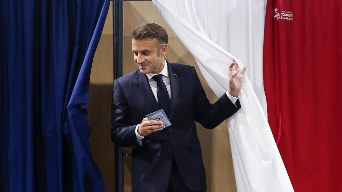 إيمانويل ماكرون يخرج من كشك اقتراع في الجولة الثانية من الانتخابات التشريعية الفرنسية المبكرة التي دعا إليها  (7/7/2024 فرانس برس)