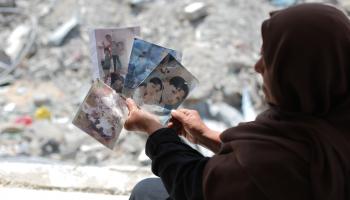 أُمّ فلسطينية تحمل صور أطفالها الذين استشهدوا في غارات على مخيّم البريج بغزّة، 18 حزيران/ يونيو 2024 (Getty)