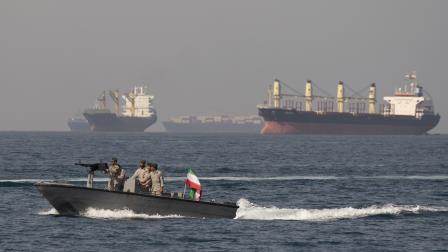 سفن تحمل شحنات نفط وسلعاً بالقرب من مضيق هرمز، خلف زورق عسكري إيراني (مرتضى نيكوبازل/Getty)