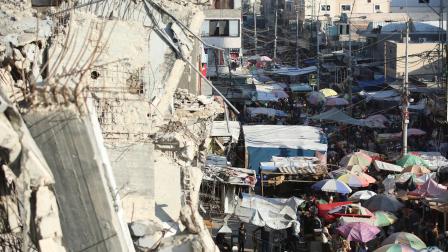 فلسطينيون يتسوّقون بين مبانٍ مدمرة في غزة (حسن الجدي/الأناضول)